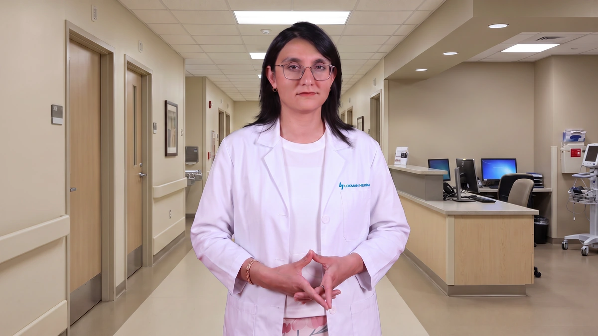 Doç. Dr. Cemile Özsürekçi, hastane koridorunda beyaz önlüğüyle